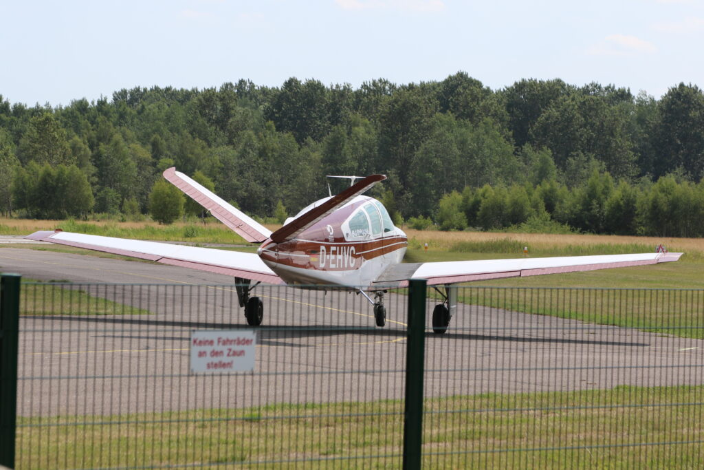 Foto taget snett bakifrån av ett taxande enmotorigt propellerflygplan, modell Beechcraft 35 Bonanza. Den ovanliga V-formade stjärten syns tydligt.