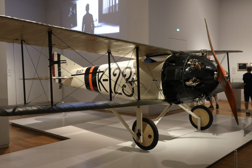 Ett litet flygplan i en museiehall. Det är ett enmotorigt biplan med öppen cockpit.
