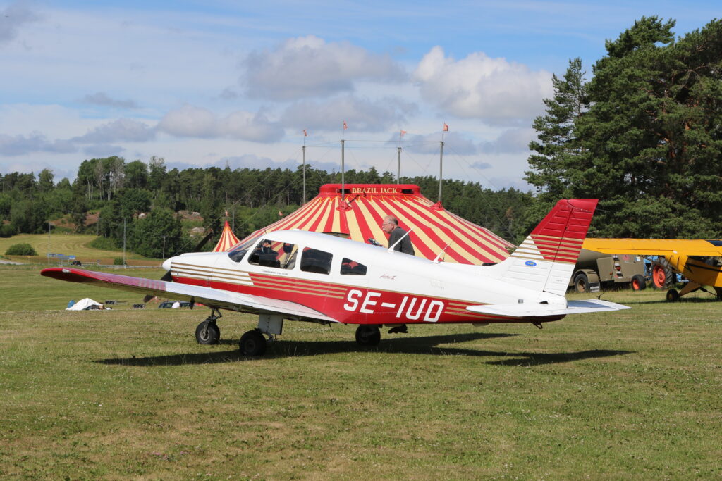 En PA-28 parkerad på kortklippt gräs framför ett stort cirkustält.