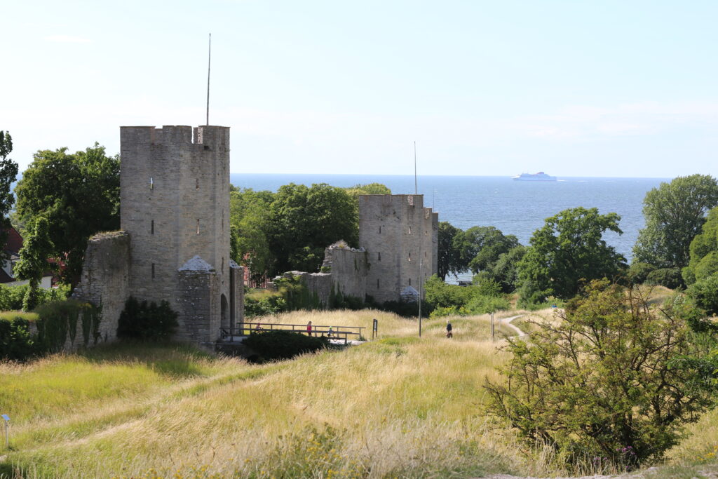 Utsidan av en bit av Visby stadsmur, med en Gotlandsfärja ute på havet i bakgrunden.
